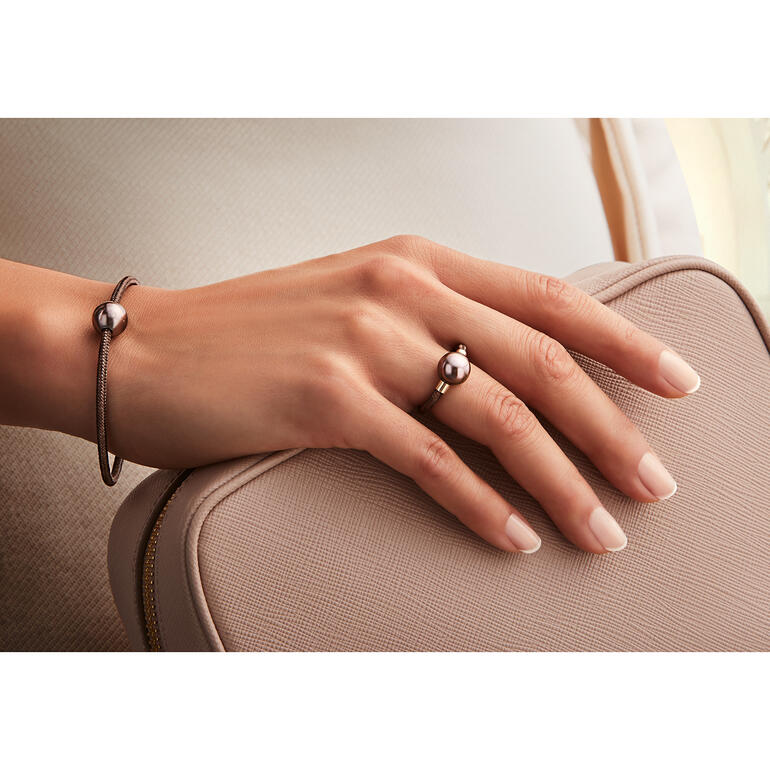 Tahiti-Armspange oder -Ring, roségold Hand, die eine roségoldene Armbänder und Ring mit schwarzer Perle auf einer Tasche hält.