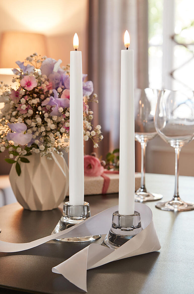 Zwei LED-Stabkerzen in einer dekorativen Umgebung neben Blumen.