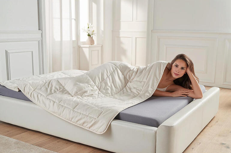 Frau liegt unter Hanf-Ganzjahresdecke auf einem Bett.