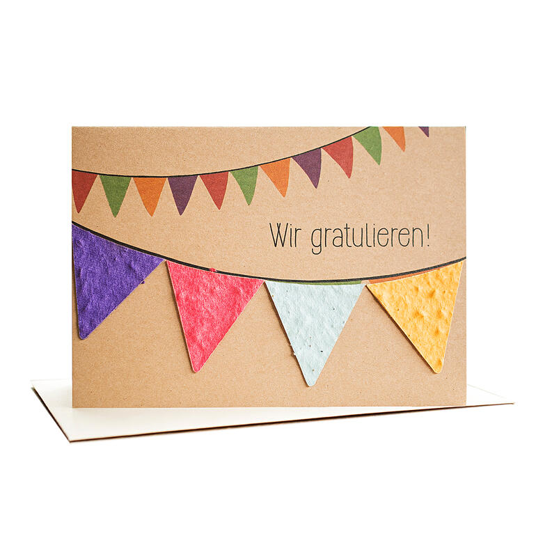 Grußkarte mit bunten Wimpeln und dem Text 'Wir gratulieren!' auf einem Tisch.