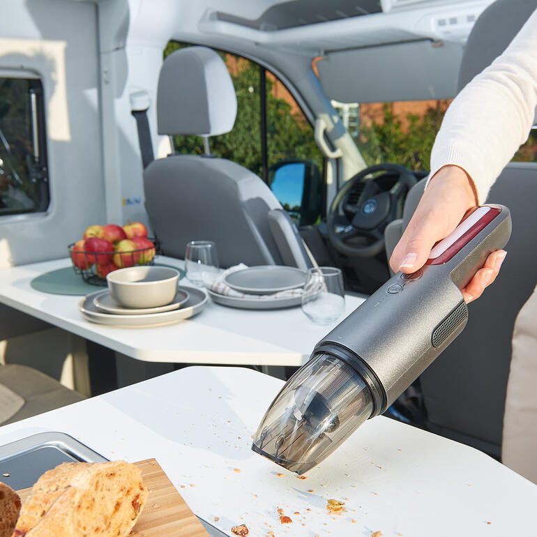 Kompakter KFZ-Sauger, benutzt in einem Wohnmobil, reinigt den Tisch.