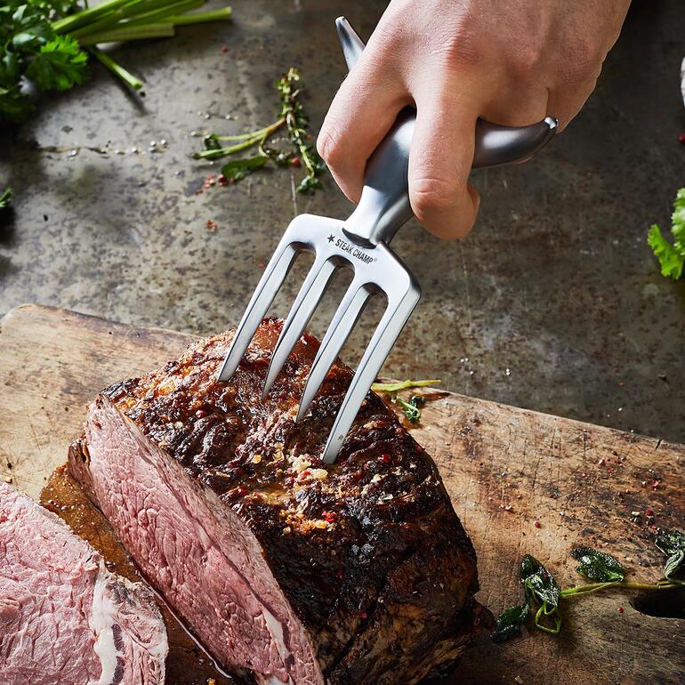 Mühelos spießen Sie mit den starken Zinken auch schwergewichtige Fleischstücke auf. Hand hält Bull Fork, um ein Stück Fleisch zu schneiden.