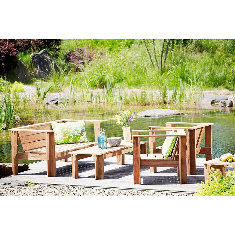 Gartenmöbel aus recyceltem Teakholz neben einem kleinen Teich in der Natur.