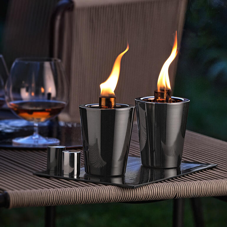Tischfackeln auf einem Tisch in einem Außenbereich mit Cocktailglas im Hintergrund.