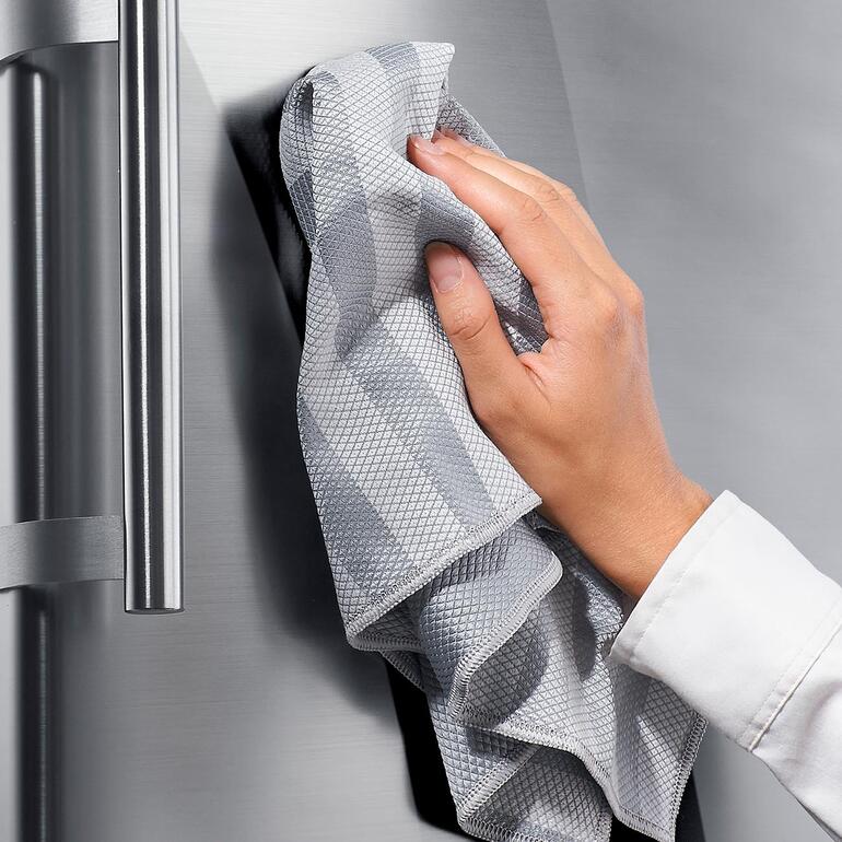 Universaltücher, 10er-Set Händchen reinigt einen Edelstahlkühlschrank mit einem grauen Universaltuch.