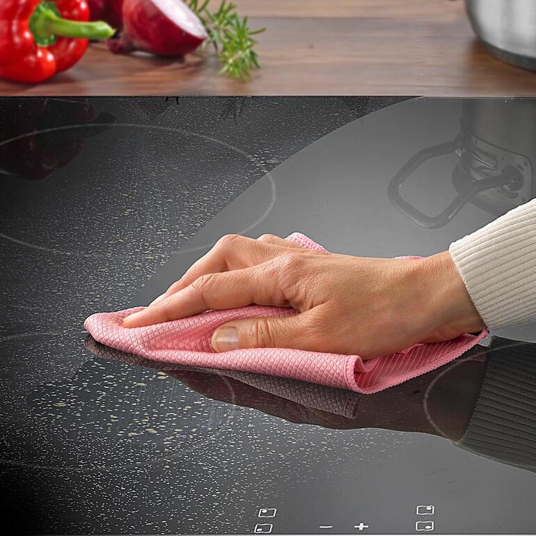 Hand wischt mit einem Fettweg-Tuch über ein Kochfeld.
