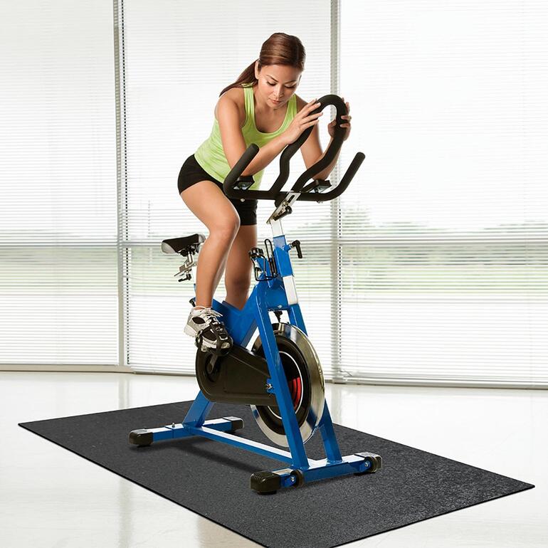 Frau auf einem Spinning-Bike auf einer Recycling-Bodenschutzmatte.