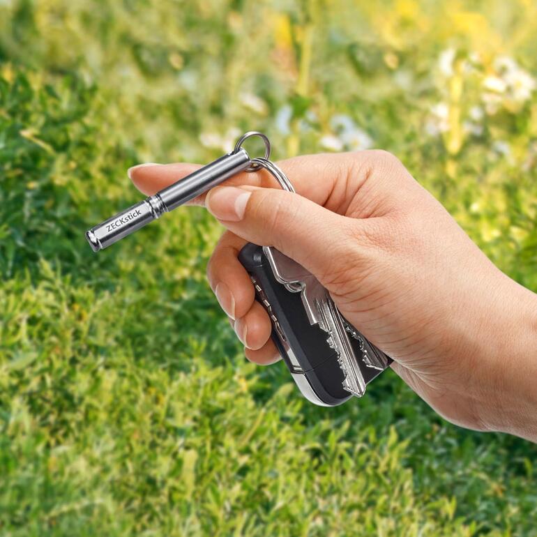 Hand hält ZECKstick und schwarzen Schlüsselbund im Freien.