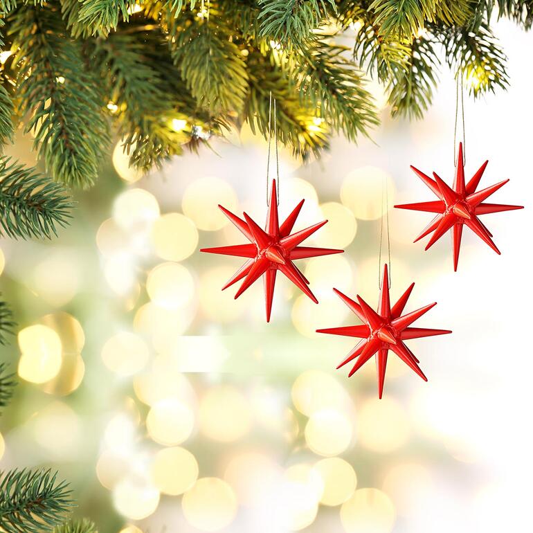 Rot Drei rote Seiffener Weihnachtssterne hängen an einem dekorierten Weihnachtsbaum.