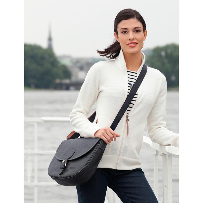 Frau mit schwarzer Stewardess-Tasche am Wasser.