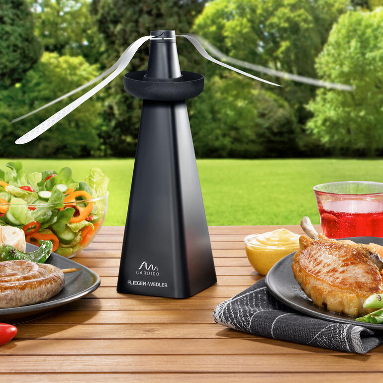 Fliegenwedler mit Wespenverdufter auf einem Tisch mit Grillgerichten.