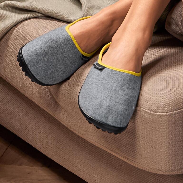Zwei graue Wollfilz-Hausschuhe leguano® auf einem Sofa.