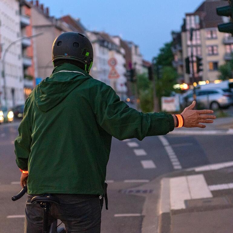 Dank zusätzlicher LED-Leuchten im Armband sind Sie für andere Verkehrsteilnehmer bei Dämmerung und Dunkelheit besser sichtbar. Radfahrer mit Leuchtarmband, der ein Handzeichen gibt.