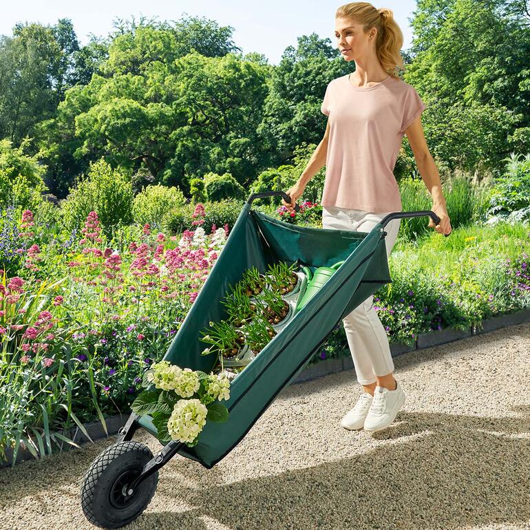 Frau trägt eine faltbare Schubkarre mit Pflanzen durch den Garten.