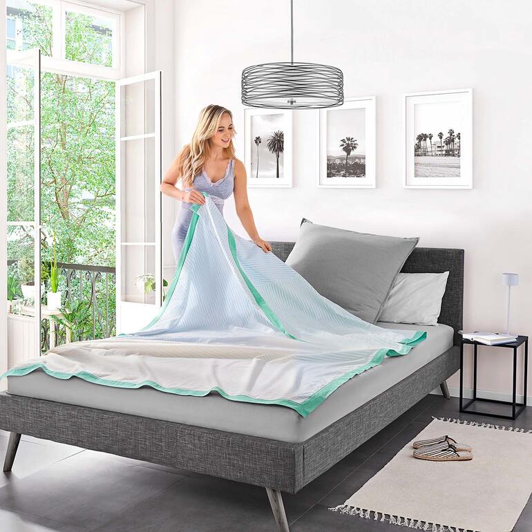 Frau faltet die Breezyblanket auf einem Bett.