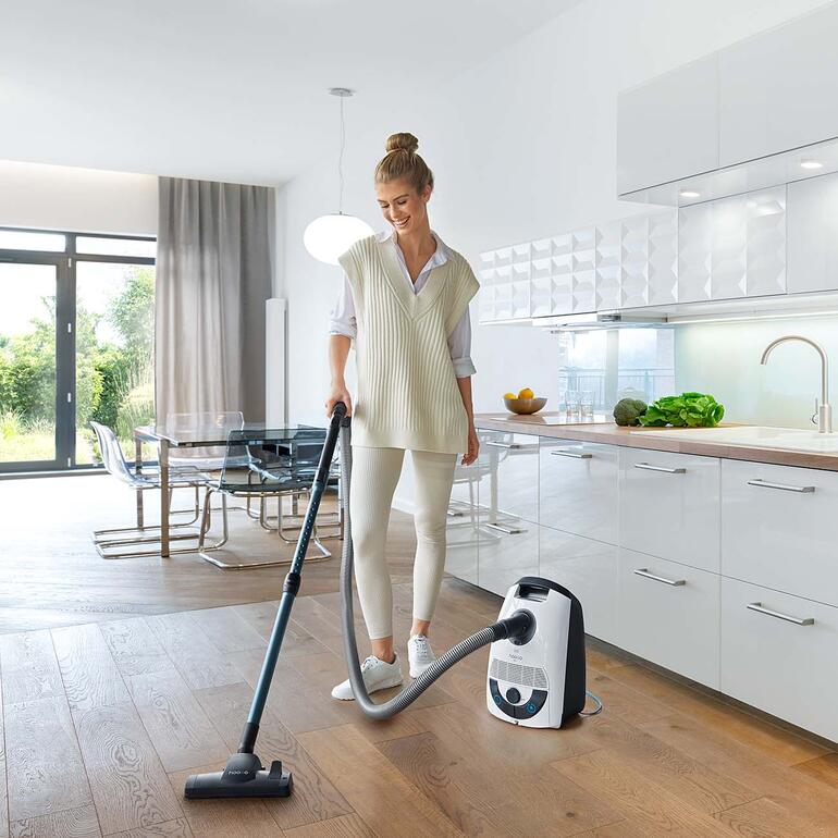 Frau verwendet einen Bodenstaubsauger im modernen Küchenbereich.