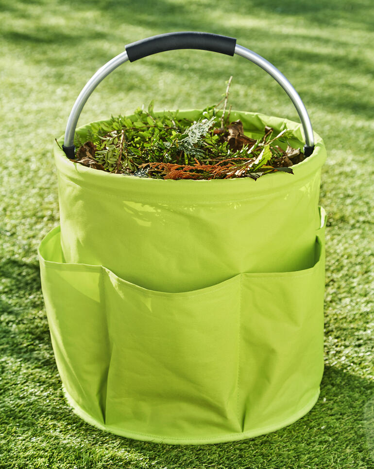 Perfekt ausgestattet mit extra großem 28 l-Mittelfach, 6 geräumigen Außentaschen und kräftigem, gepolsterten Alugriff. Garten Caddy gefüllt mit Pflanzenabfällen auf grünem Gras.