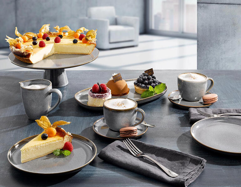 Geschirrserie mit verschiedenen Tellern, Tassen und Kuchen auf einem Tisch.
