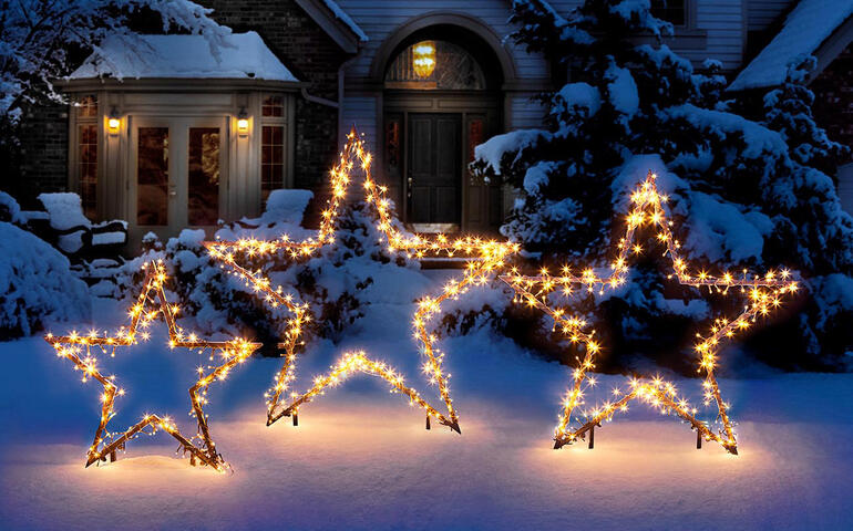 Drei leuchtende LED-Sterne im verschneiten Garten.