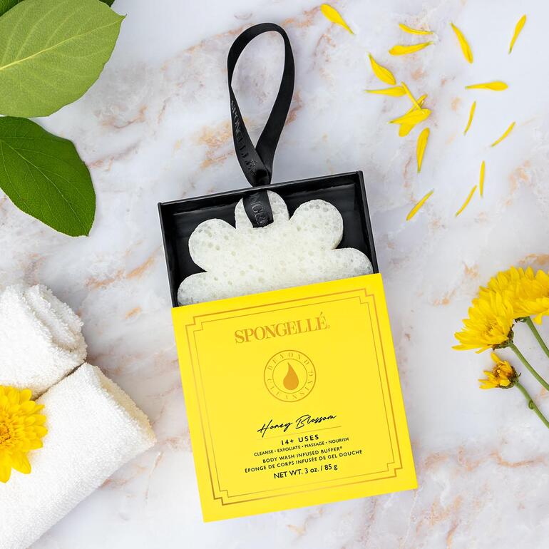Spongellé Beauty-Schwamm in einer gelben Verpackung zusammen mit Naturdekoration.