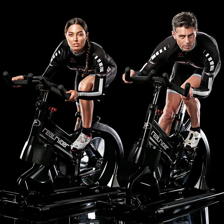 Zwei Menschen auf RealRyder Indoor-Bikes, fokussiert beim Training.