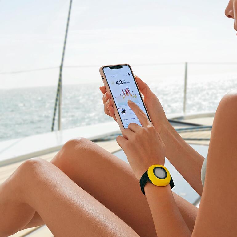 UV-Bodyguard am Handgelenk einer Person mit Smartphone auf einem Boot.