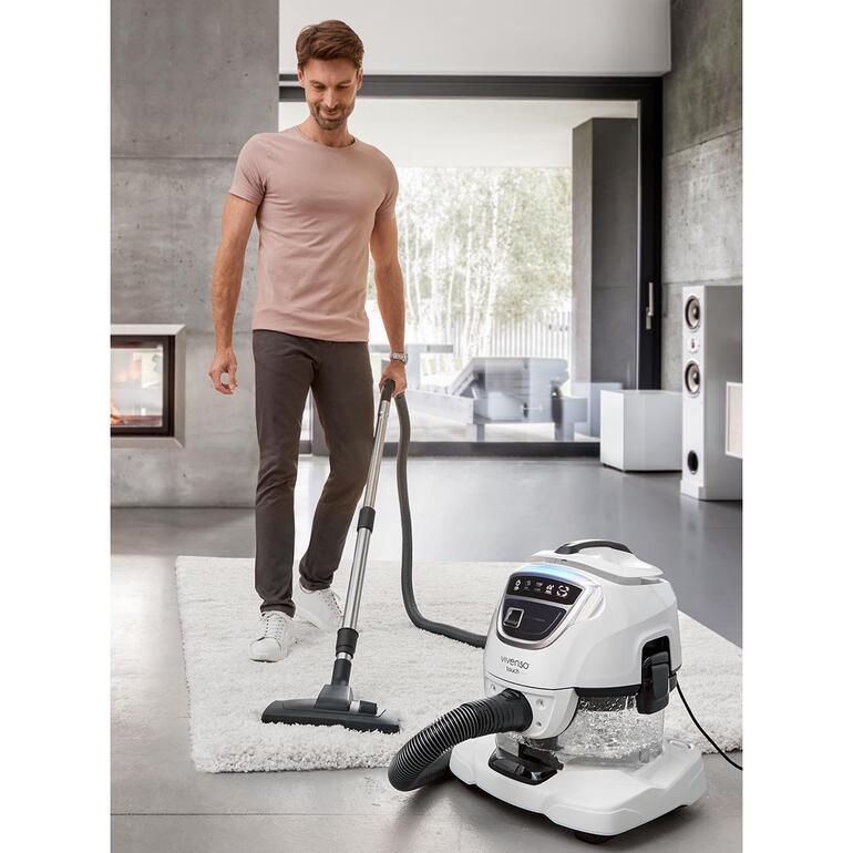 Mann mit Staubsauger auf Teppich in modernem Wohnraum.