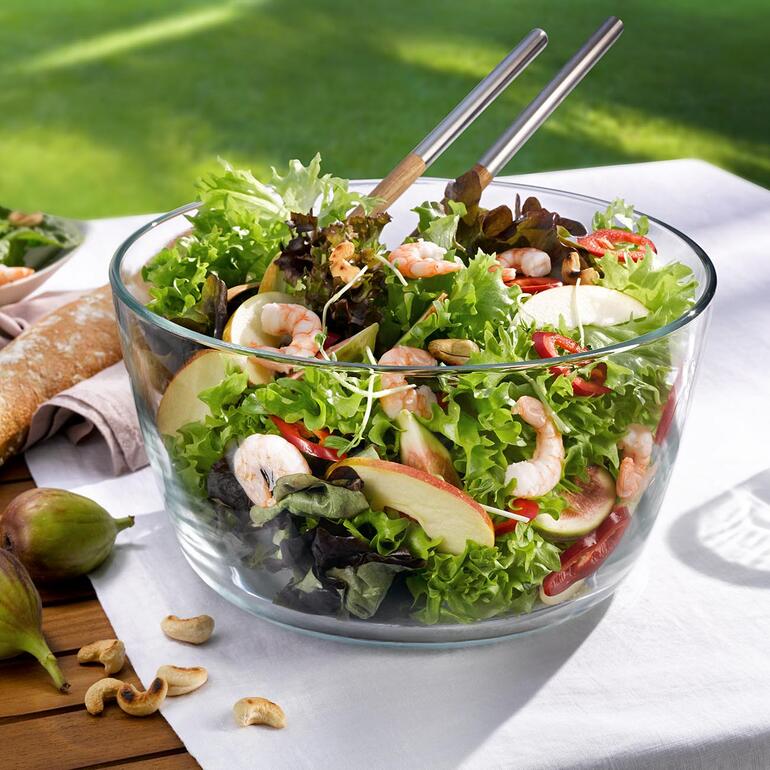Dank herausnehmbarem Schleuderkorb servieren Sie den gespülten Salat direkt in der edlen Schüssel aus kristallklarem Borosilikatglas. Schüssel mit frischem Salat auf einem Tisch im Freien.