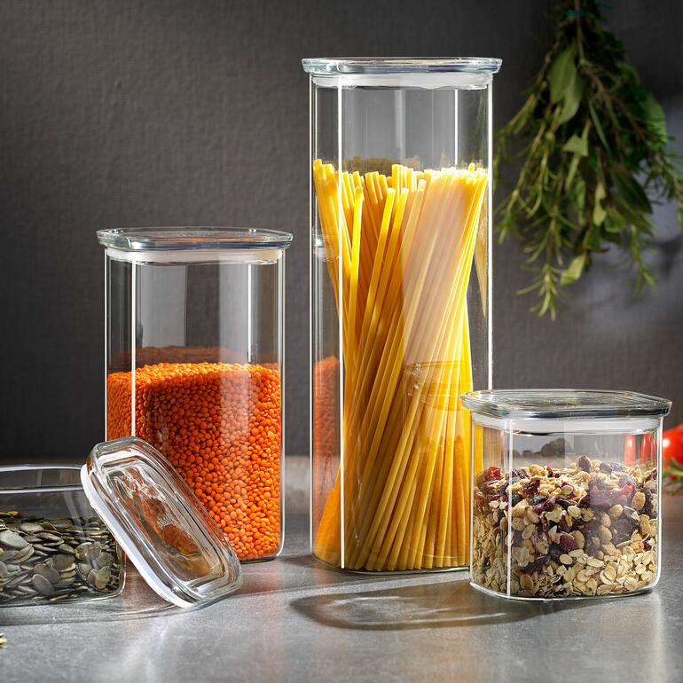 Vorratsgläser mit Glasdeckel, gefüllt mit Linsen, Spaghetti und Müsli auf einem Tisch.