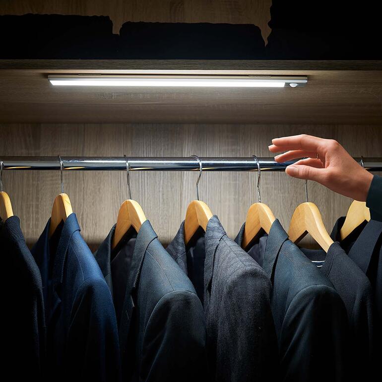 Variable Akku-Lichtleiste im Kleiderschrank, während eine Hand einen Anzug aufhängt.