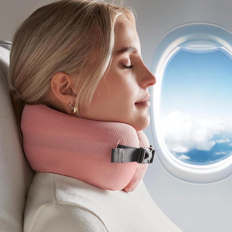 Frau mit rosa Komfort-Reisekissen, entspannt am Fenster im Flugzeug.