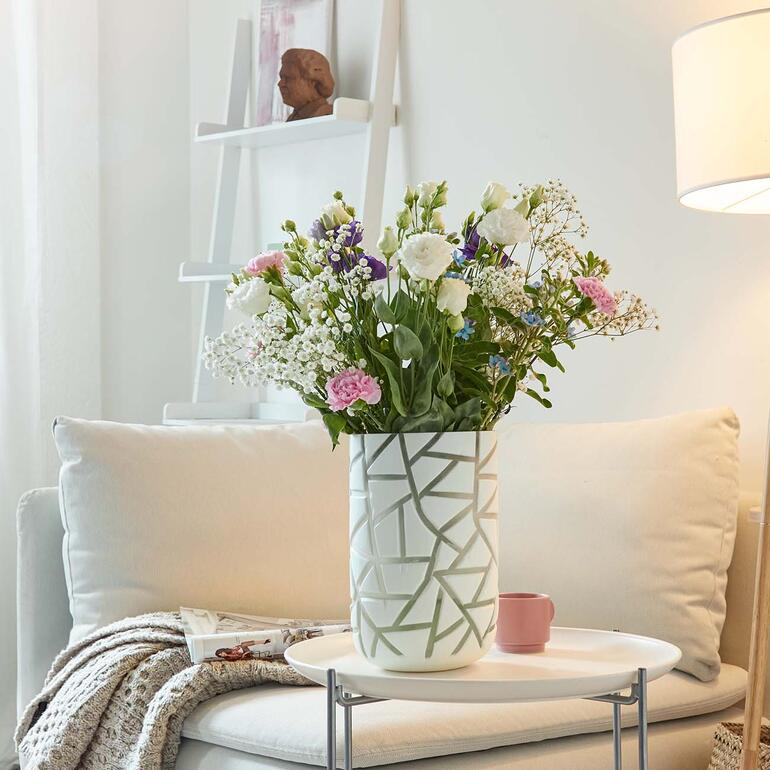 Vase mit bunten Blumen und Keramikutensilien auf einem Tisch