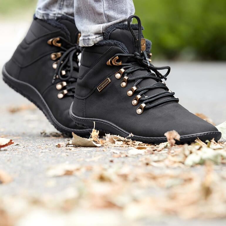 Mit diesen winterwarmen Schnürboots genießen Sie das besonders freie, natürliche Laufgefühl auch an kalten Tagen – im Alltag, beim Einkaufsbummel, Städtetrip, Wald-Spaziergang, ... Schwarze Winter-Schnürboots mit goldenem Detail und Schnürsenkeln auf grauem Boden.
