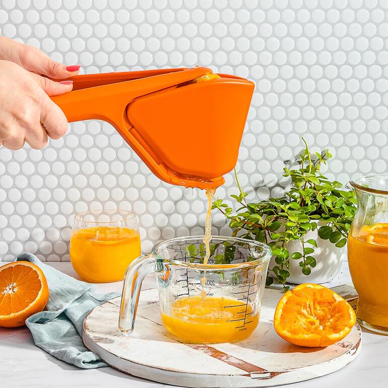 Faltbare Zitruspresse in Orange, die Saft in ein Glas drückt.