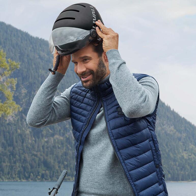 Das Erfolgsmodell im coolen urbanen Design ist jetzt zusätzlich mit einem Visier ausgestattet. Mann setzt sich den Livall L23 E-Bike Helm auf einem Berggipfel auf.