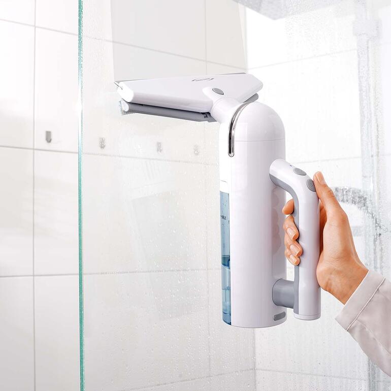 Hand hält einen weißen Akku-Fensterreiniger in einem Badezimmer.