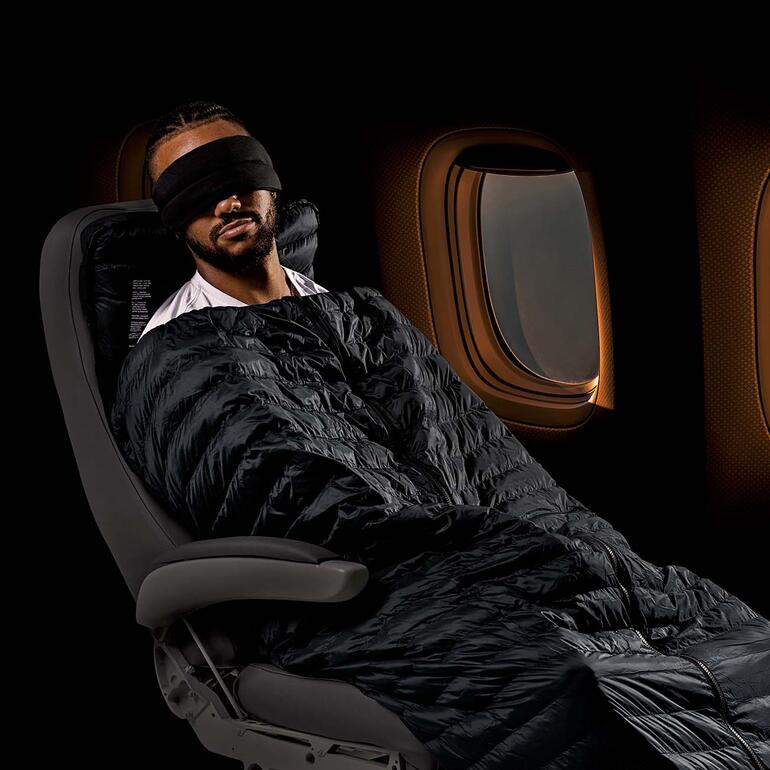 Mann mit Schlafmaske entspannt in einem Flugzeugsitz