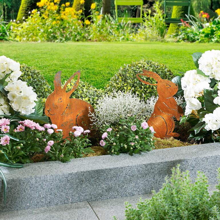 Zwei Gartenstecker in Hasenform aus Metall im Blumenbeet platziert.