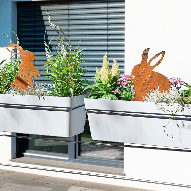 Nach einer Weile draußen, bildet sich auf den Hasenmotiven in kurzer Zeit eine feine, fellähnliche Rostschicht. Hasen-Gartenstecker in Blumentöpfen auf einem Balkon dekoriert.