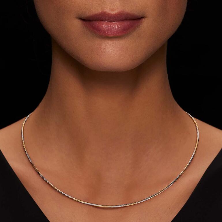 Das feine bi-color Design gibt dem Collier dezent lebendiges Strukturspiel. Frau trägt ein Bi-color Kabelcollier, sichtbar im Dekolleté.