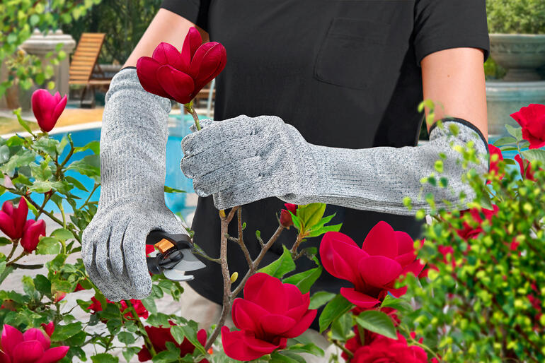 Gärtnerin mit Safety-Gartenhandschuhen schneidet eine Blume.