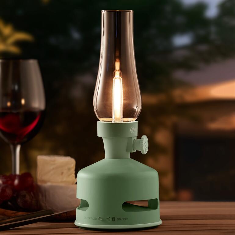 LED-Öllampe in mintgrün mit Kerze im Freien auf einem Tisch.