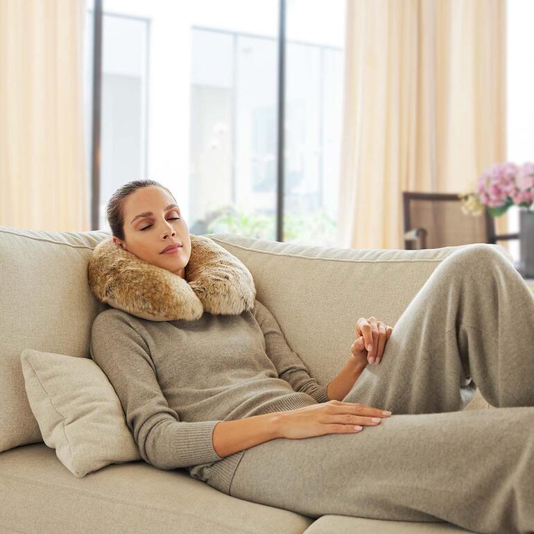 Frau entspannt mit Faux-Fur-Nackenhörnchen auf dem Sofa