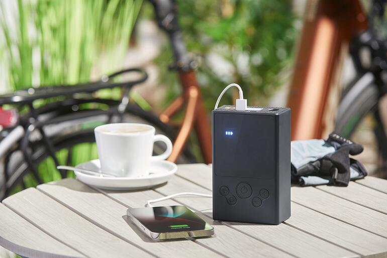 In einem auch 5.400 mAh Lithium-Ionen-Powerbank für Handy, Tablet und andere Mobilgeräte. Akku-Kompressor-Luftpumpe lädt ein Smartphone auf einem Tisch.