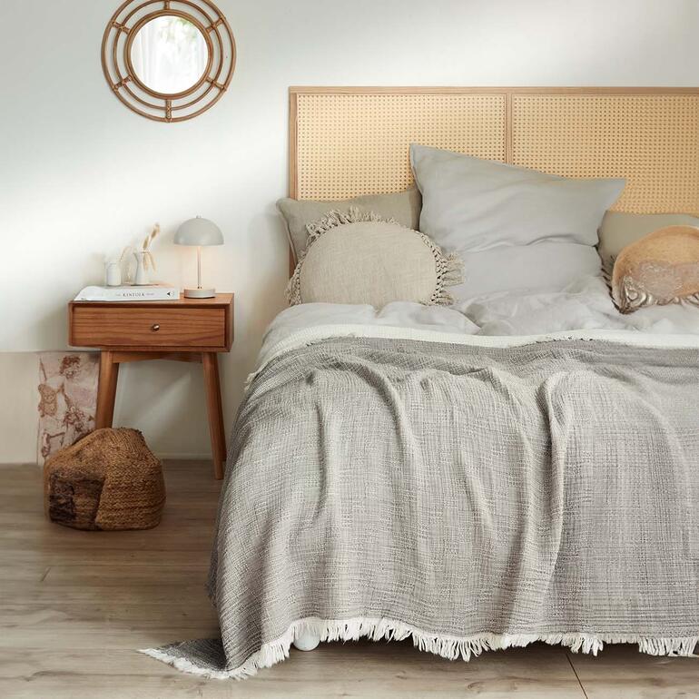 Musselindecke in grau auf einem Bett mit Kopfteil und Kissen.