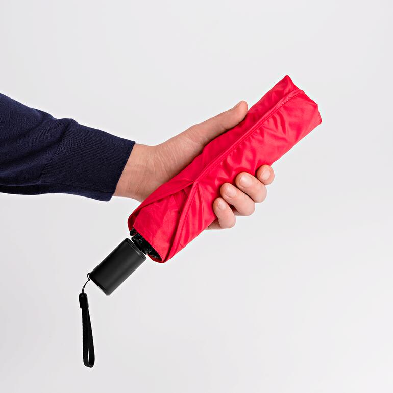 Zusammengefaltet genauso handlich klein wie ein normaler Taschenschirm. Hand hält einen zusammengelegten roten Taschenschirm