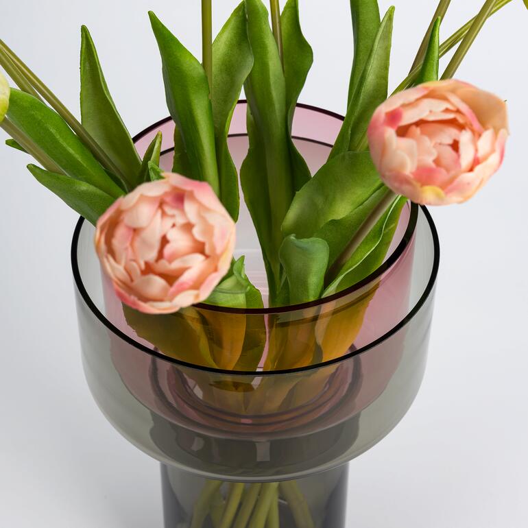 In die graue Glas-Manschette setzen Sie das zweite, purpurfarbene Glas – je nach Bedarf mit der schlanken oder der breiten Öffnung nach oben. Vario-Glasvase mit Tulpen und grünem Blattwerk, im Mittelpunkt des Bildes.
