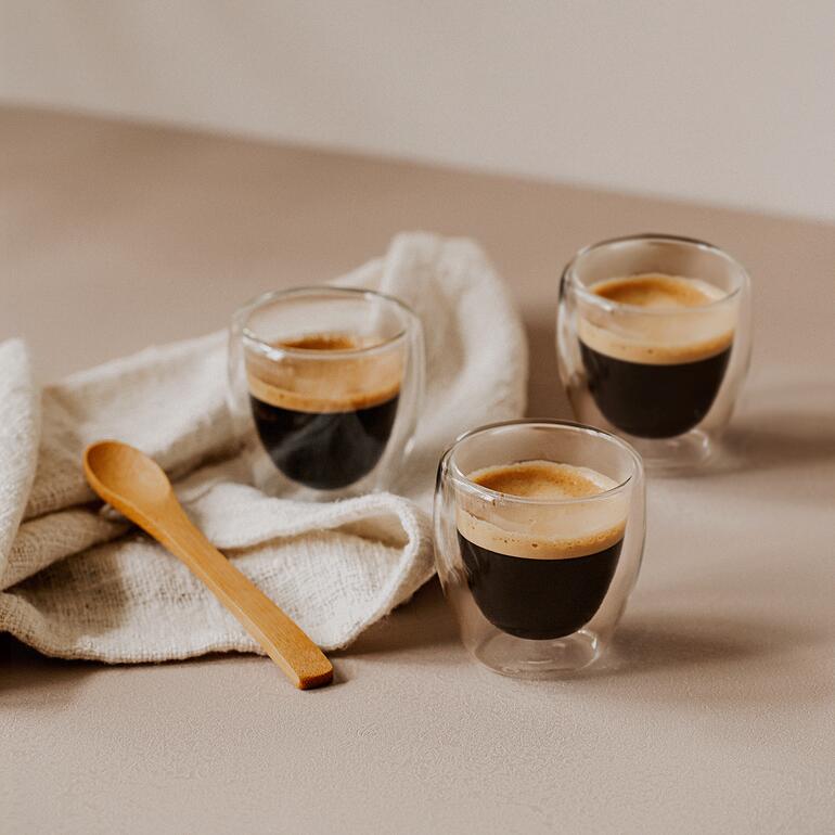 Espresso (80 ml, 6,5 cm H) Drei elegante Espresso-Thermogläser mit frischem Espresso auf einem Tisch.
