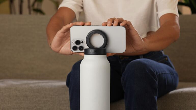 Person hält eine 2-in-1-Trinkflasche, während ein Smartphone darauf balanciert.