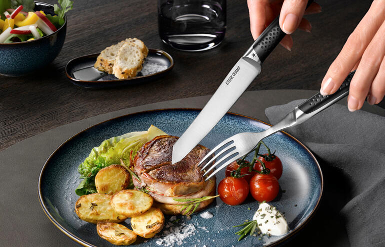 Hand, die mit Steak-Besteck Prime Rib auf einem Teller in ein Stück Steak schneidet.